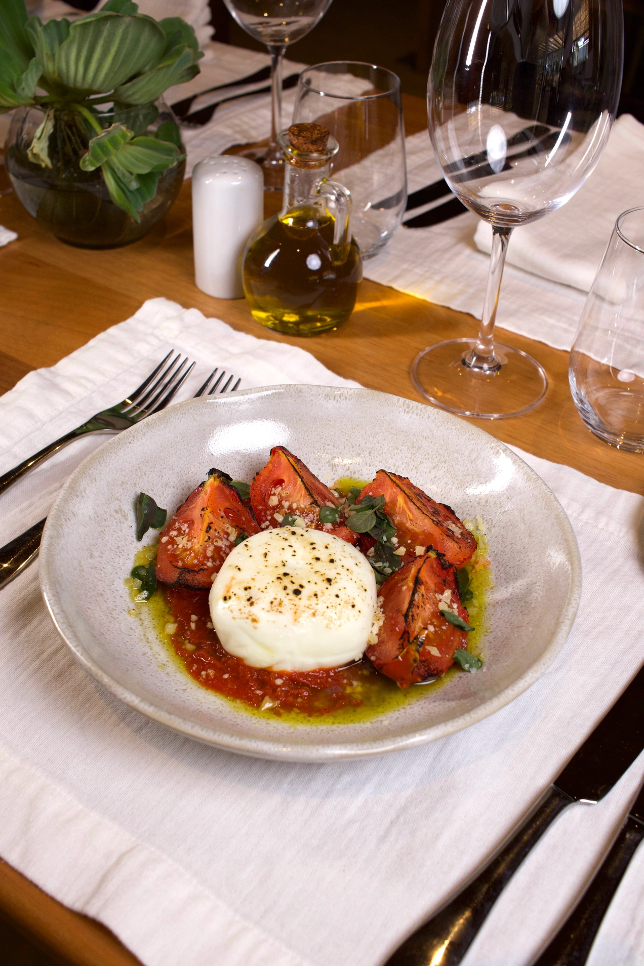 Burrata com tomates grelhados, molho vermelho e azeite em mesa posta.
