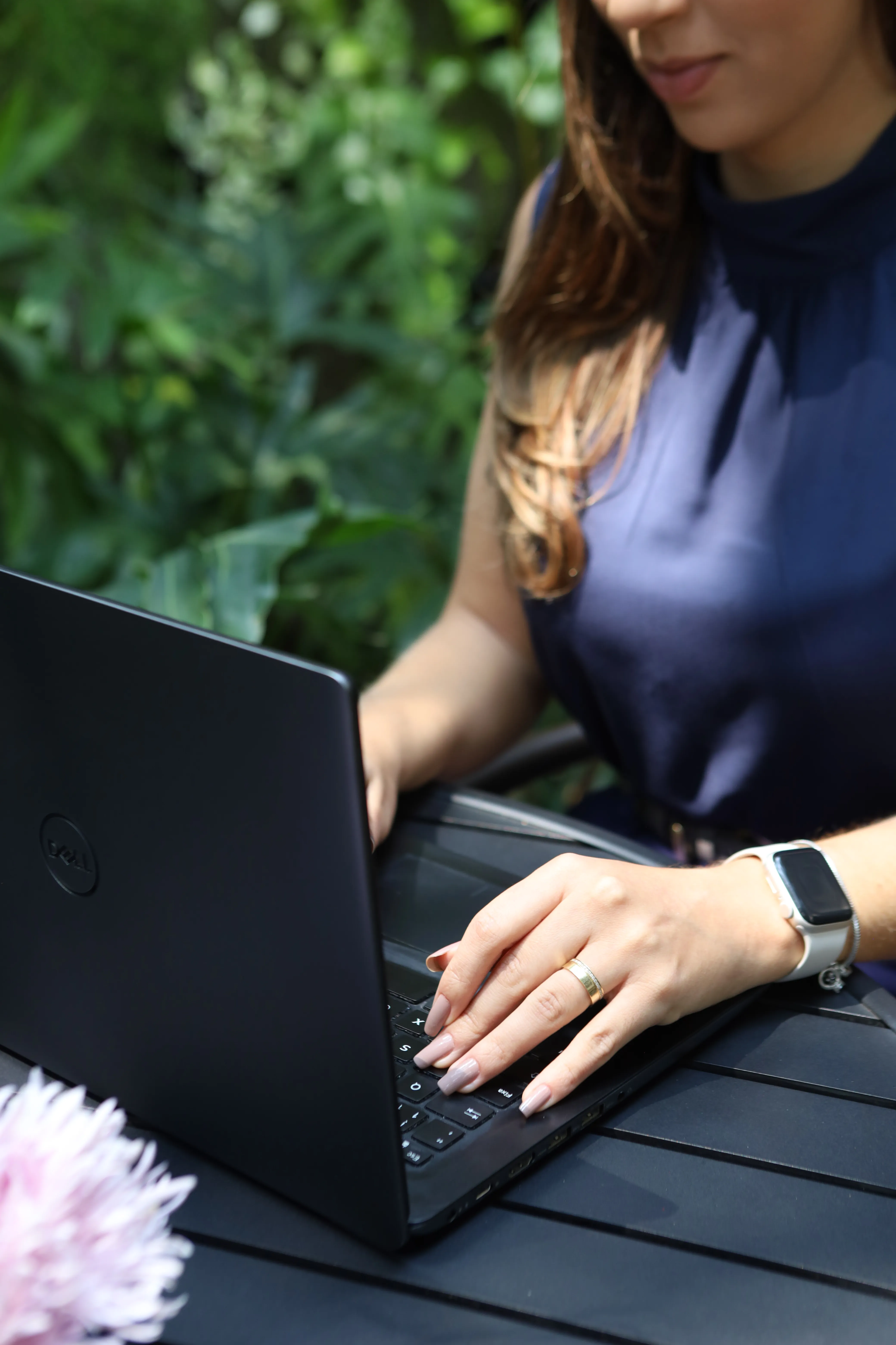 Profissional trabalha em um notebook ao ar livre, cercada por plantas.