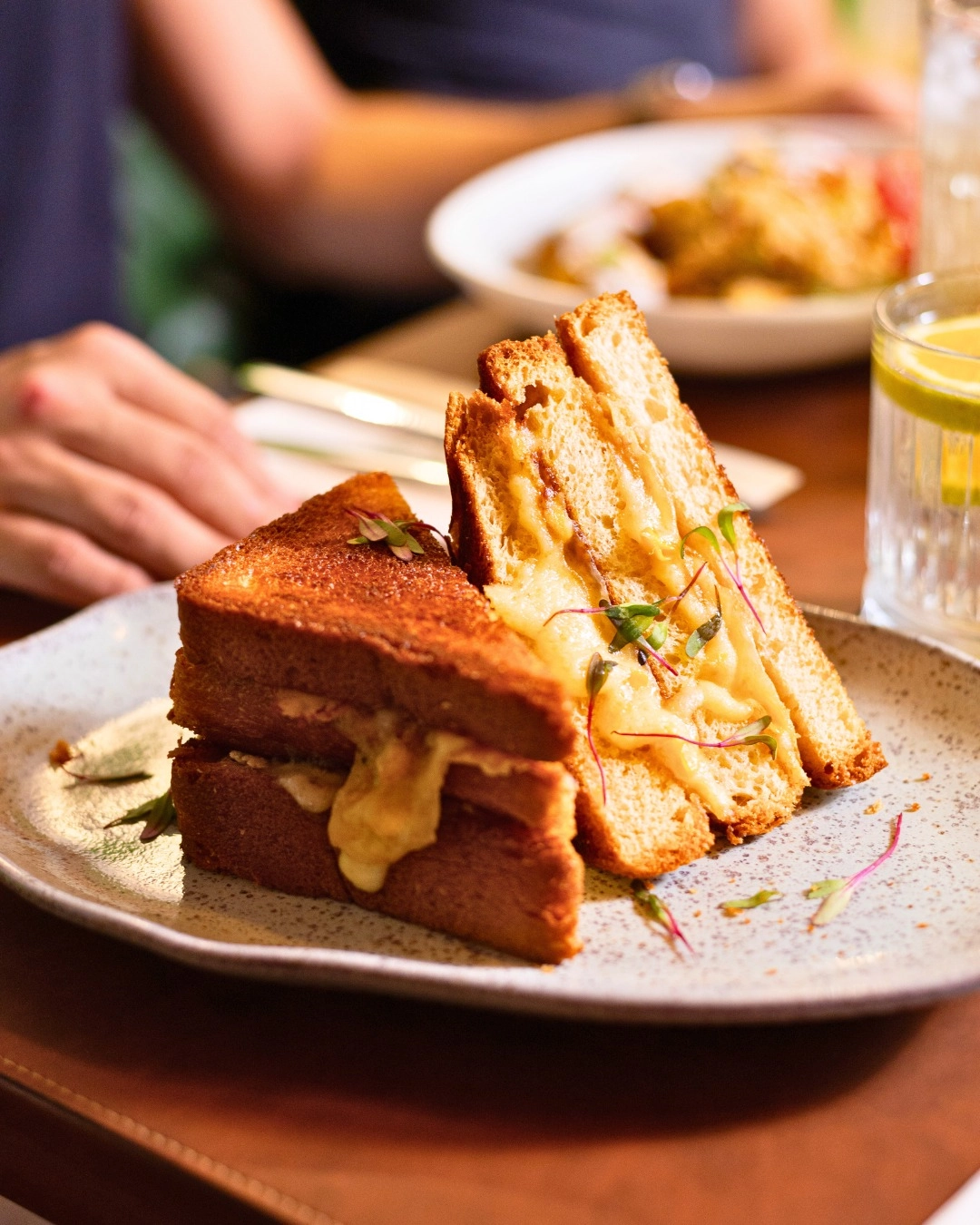 Sanduíche tostado com queijo derretido servido em prato de brunch.